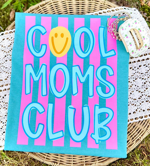 Cool Moms Club graphic tee with pink stripes, teal lettering, and yellow smiley face on a turquoise shir