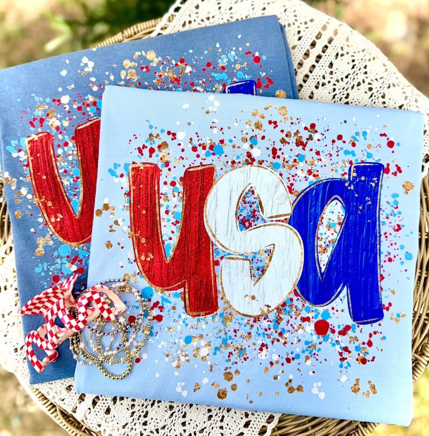 Light blue patriotic t-shirt with bold USA lettering in red white and blue and paint splatter design
